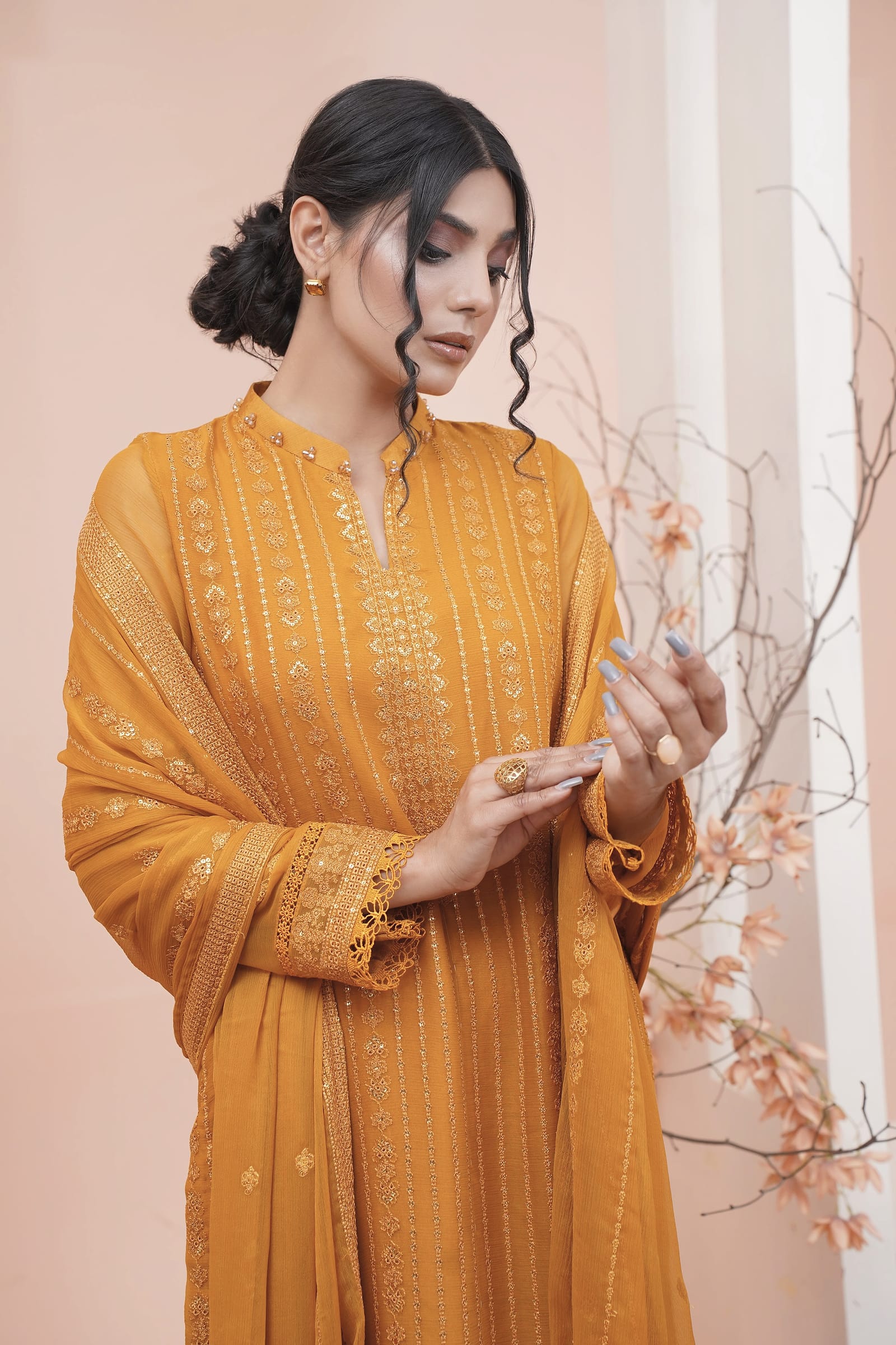 A woman is close in a peach-lit room, wearing a saffron-mustard long coat-front kurta set.