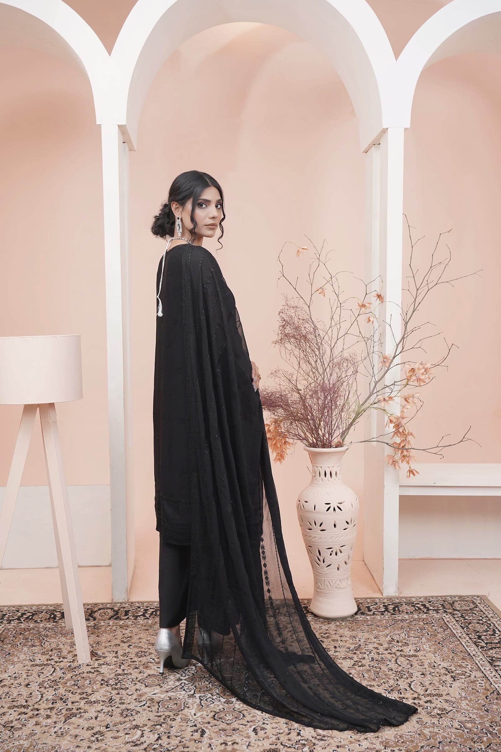 A woman stands with her back turned, the dupatta trailing, wearing a black sheer kurta set with an embroidered placket and a black dupatta.