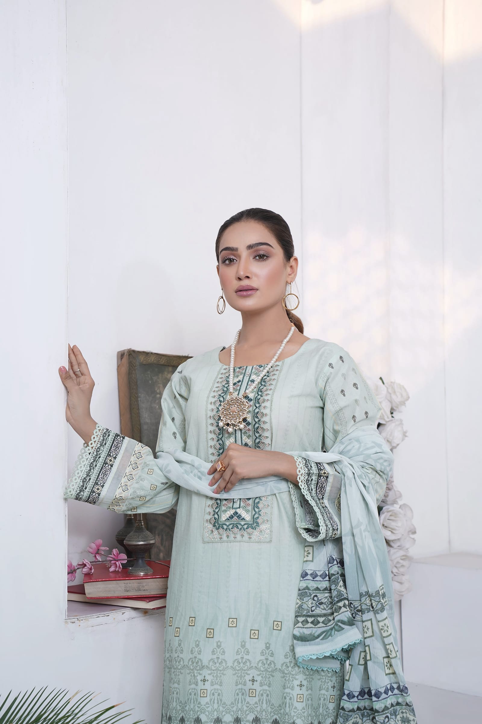 A woman is close in a white room, wearing a pale mint kurta set with an aqua and grey embroidered yoke and a long dupatta.