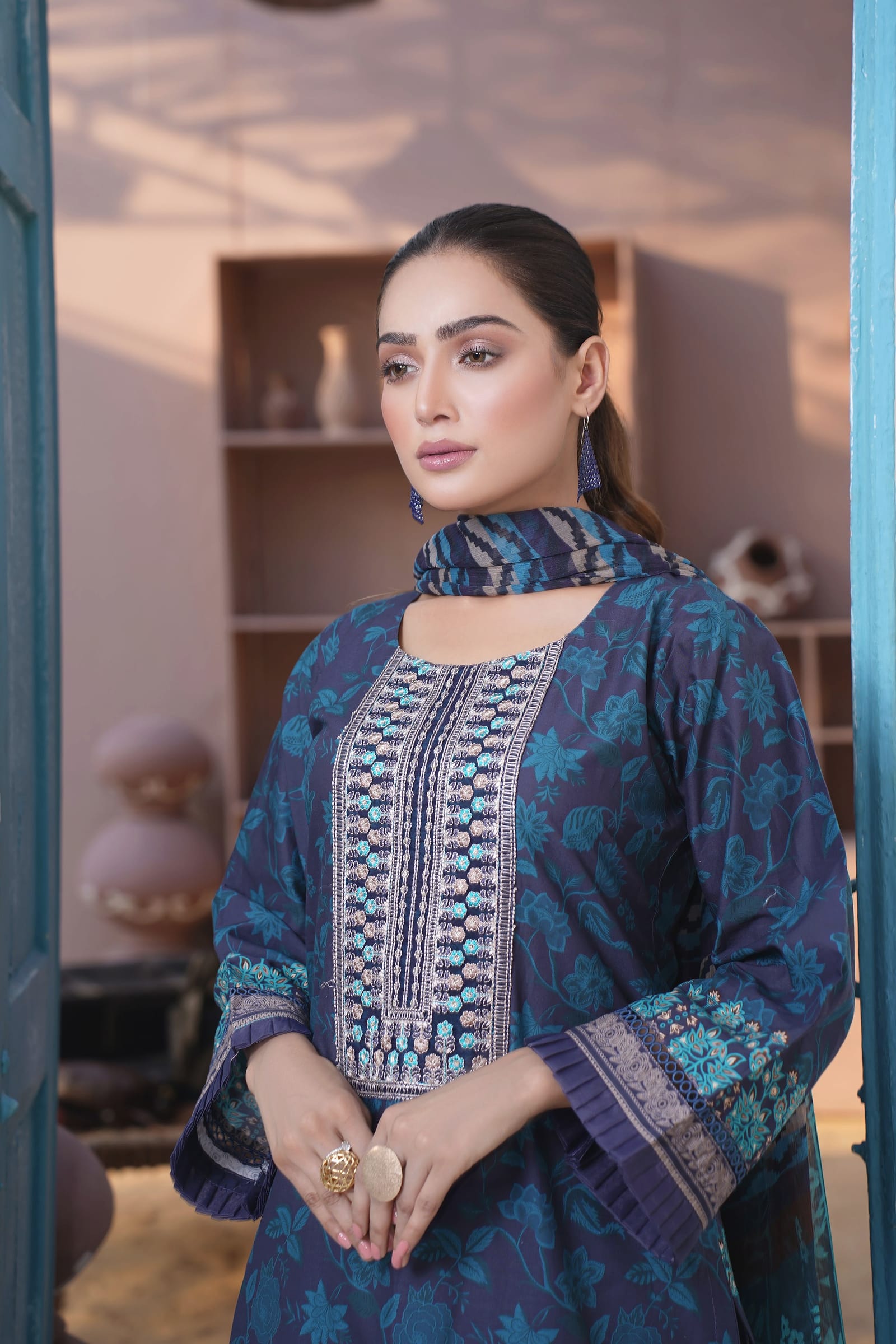 A woman is close in front of a blue door, wearing an ink-navy kurta set with an aqua floral print and a wave-print dupatta.