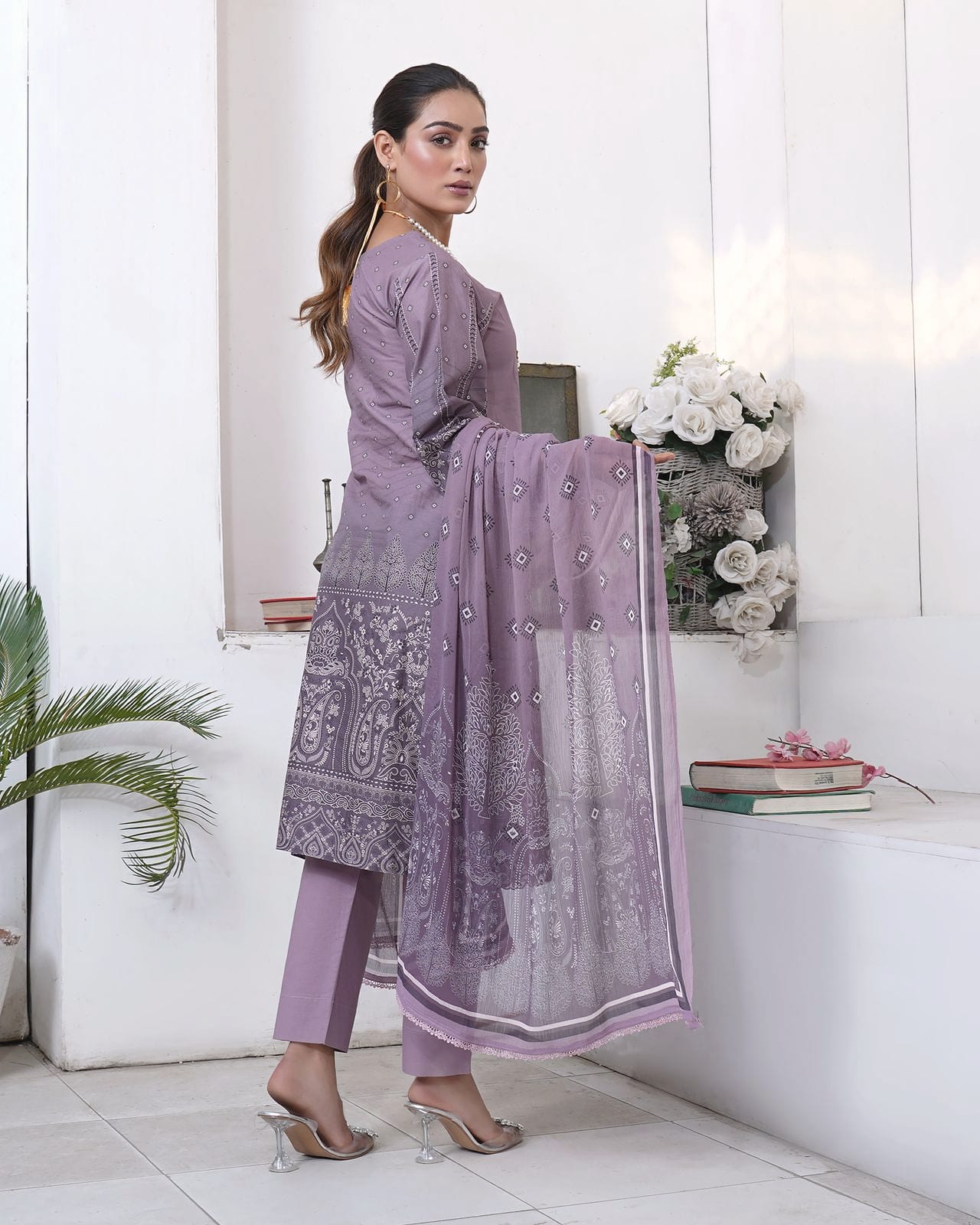 A woman stands with her back turned, the dupatta behind her, wearing a dusty lilac kurta set with a tonal print.